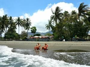 Lauhata Beach Escape — guests in the surf with palm-fringed beach behind